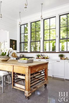 an old wooden table in the middle of a kitchen with lots of windows and potted plants on it