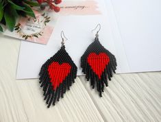 red and black beaded heart earrings on white wooden table next to card with envelope