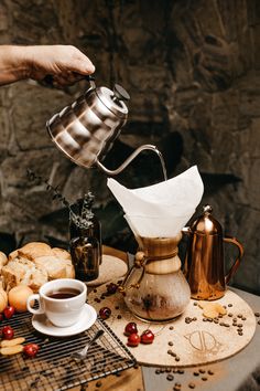 a person pours coffee into a cup on a table next to bread and fruit