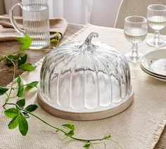 a glass cake dish sitting on top of a table next to wine glasses and plates