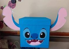 a blue box with an angry face and big teeth on it's head, sitting in front of a wall