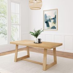 a wooden table sitting on top of a white rug next to a painting and potted plant