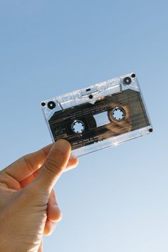 a person holding up an old fashioned cassette in front of a blue sky with no clouds