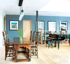 a dining room with blue walls and wooden furniture in front of a piano, chandelier, and bookshelves