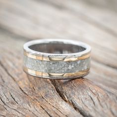 a close up of a wedding ring on top of a piece of wood with gold and silver inlays