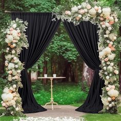 an outdoor wedding ceremony with black drapes and white flowers on the arch, surrounded by greenery