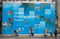 people walking and riding bikes in front of a large blue sign that says health financial systems forum