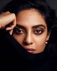 a close up of a person wearing a black turtle neck sweater and gold hoop earrings