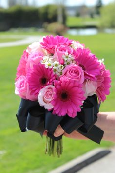 a person holding a bouquet of pink flowers in their hand with grass behind them on a sunny day