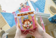 a hand holding up a small box filled with cereal and other items in front of a house