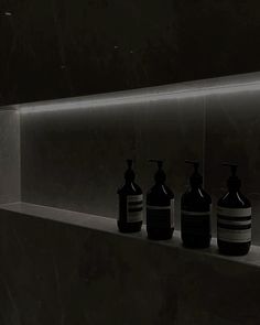 three soap dispensers are lined up on a shelf in the dark room