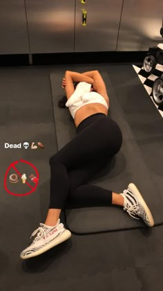 a woman laying on top of a black mat in a room with white shoes and no shirt