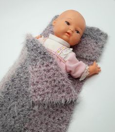 a baby doll laying on top of a gray and white blanket covered in fuzzy material