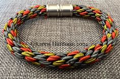 an orange, yellow and grey braided bracelet on a gray cloth with a metal clasp