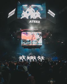 a large screen at a concert with dancers on it and people in the audience watching