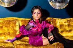 a woman sitting on top of a yellow couch in front of disco ball lights and mirrors