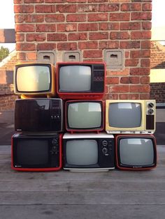 old televisions are stacked on top of each other in front of a brick wall