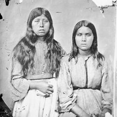 an old black and white photo of two women in native american clothing with long hair