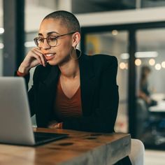 a woman sitting at a table with a laptop computer in front of her and looking off to the side