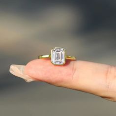 a person's hand holding a ring with an emerald stone in the middle, on top of their finger