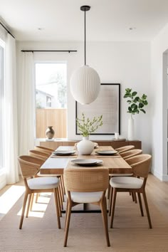 a dining room table with white chairs and a vase on it's centerpiece