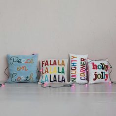 three decorative pillows are lined up against a wall with string lights on the floor below them