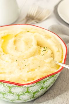 a bowl filled with mashed potatoes on top of a table next to silverware