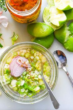 a glass bowl filled with food next to some limes and other ingredients on a table