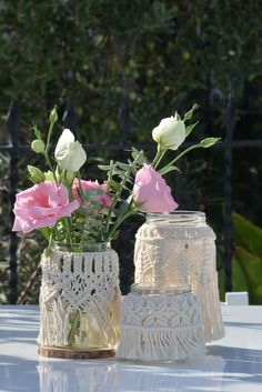 two vases with pink and white flowers in them sitting on top of a table