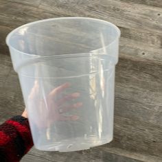 a person holding up a plastic cup with something in it's hand on a wooden surface