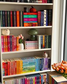 a bookshelf filled with lots of colorful books next to a vase full of flowers