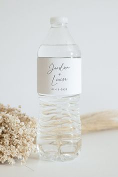 a bottle of water sitting next to some dried flowers on a white surface with the label printed out