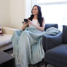 a woman sitting on a couch with a blanket over her and holding a cell phone