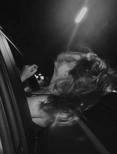 a woman sitting in the passenger seat of a car with her hair blowing back and eyes closed