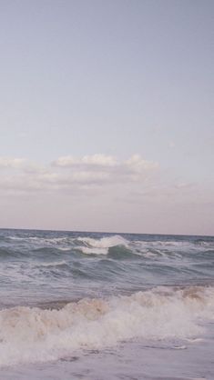 a man standing on top of a sandy beach next to the ocean holding a surfboard