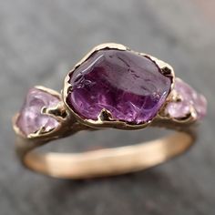 Lovely purple sapphire and pink sapphire side stones. We tumbled them at home and I hand carved this setting in wax and cast it in recycled solid 18k yellow gold using the lost wax casting process. This one-of-a-kind gemstone ring is a size 7 it can be resized up or down for you as needed. The sapphire stone measures about 8mm X 7mm and the side stones are close to 5x4mm. The band is around 2.5mm wide.Throughout all time and history in every tribe and culture all around the world crystals, miner Rough Gemstone Jewelry, Raw Pink Tourmaline, Sapphire Side Stones, Vintage Engagement Ring Settings, Yellow Gold Diamond Engagement Ring, Raw Gemstone Ring, Diamond Wedding Jewelry, Yellow Engagement Rings, Gold Statement Ring