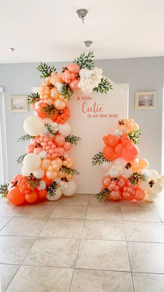 an arch made out of balloons and flowers on the floor in front of a sign