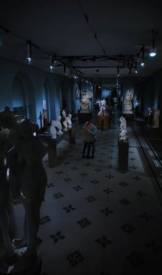 a room filled with statues and people standing around in front of them at night time