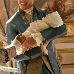 a man holding a baby in his arms while wearing a blue coat and white shirt