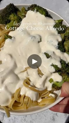 a person is holding a plate of pasta and broccoli covered in white sauce