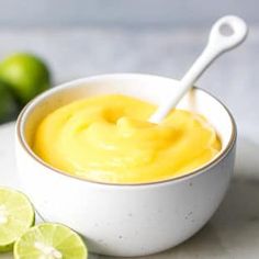 a white bowl filled with lemon custard next to limes on a table