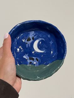 a hand is holding a blue bowl with animals painted on it and the moon in the sky