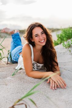 a beautiful young woman laying on top of a sandy beach next to tall grass and plants