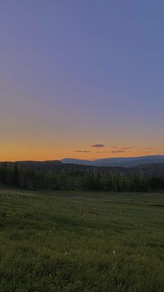 the sun is setting over an open field with mountains in the distance and trees to the side