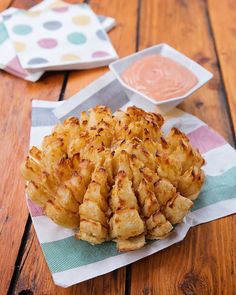 some fried food sitting on top of a wooden table next to a bowl of dipping sauce