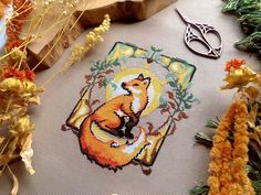 a cross - stitch fox is sitting on the ground next to some flowers and scissors