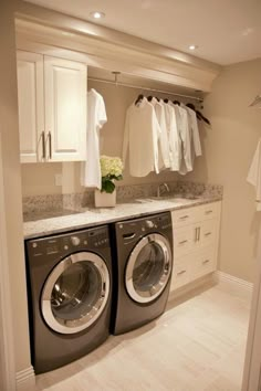 a washer and dryer in a room with white cabinets, drawers and clothes hanging on the wall