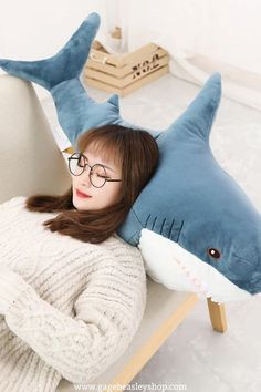 a woman wearing glasses is laying on a chair with a shark pillow