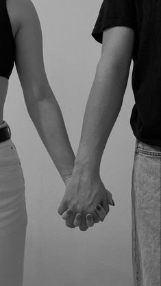 two people holding hands in front of a white wall