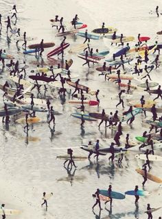 a large group of people with surfboards walking on the shore line at the beach